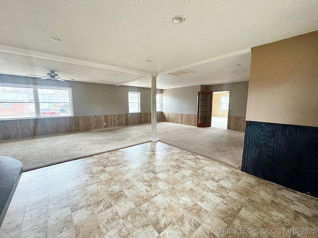 interior space featuring ornate columns, a textured ceiling, carpet flooring, wooden walls, and ceiling fan