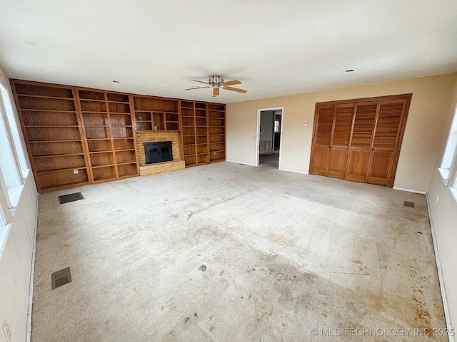 unfurnished living room featuring a brick fireplace, carpet floors, built in features, and ceiling fan