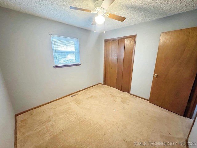 unfurnished bedroom with ceiling fan, light carpet, a textured ceiling, and a closet