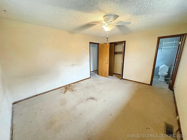 unfurnished bedroom featuring ceiling fan, ensuite bathroom, a textured ceiling, light carpet, and a closet