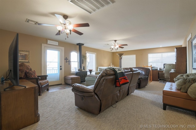 carpeted living room featuring ceiling fan, a wood stove, and a healthy amount of sunlight