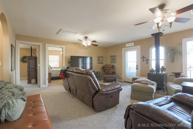 living room featuring ceiling fan, a wood stove, and light carpet