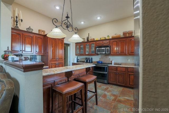 kitchen featuring a kitchen breakfast bar, decorative light fixtures, stainless steel appliances, and light stone countertops