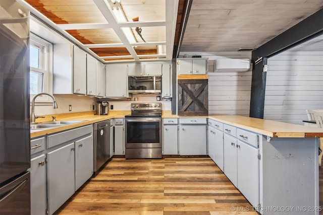 kitchen with sink, light hardwood / wood-style flooring, appliances with stainless steel finishes, a wall mounted AC, and kitchen peninsula