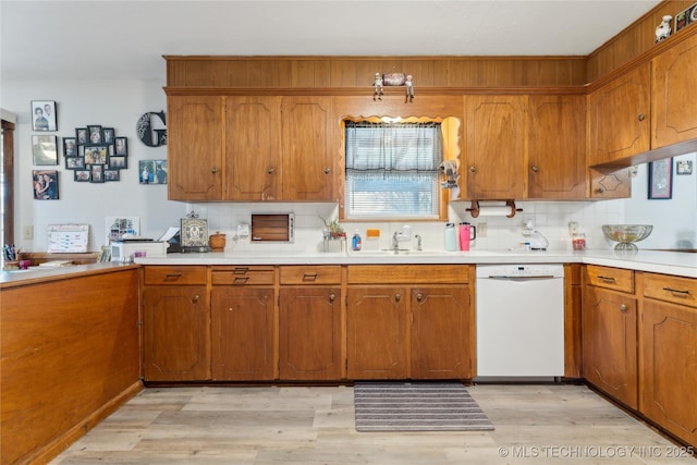 kitchen featuring white dishwasher, backsplash, sink, and light wood-type flooring