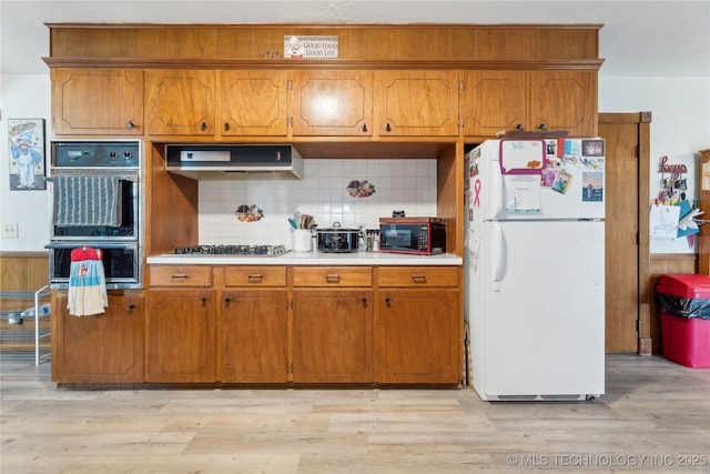 kitchen with white fridge, double oven, light hardwood / wood-style floors, and range hood