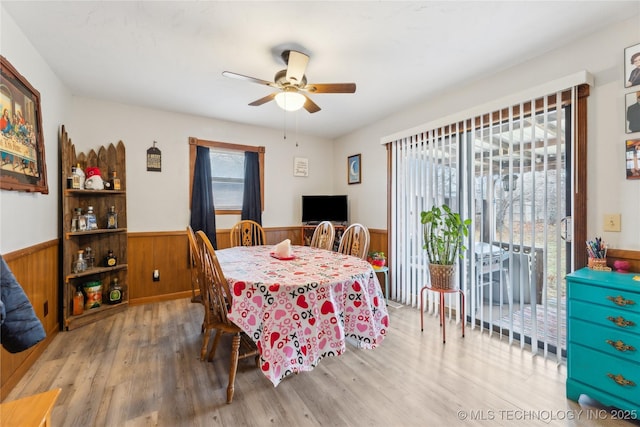 dining area with light hardwood / wood-style flooring, wooden walls, and ceiling fan