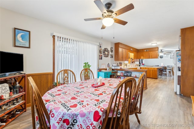 dining room with ceiling fan, wooden walls, and light hardwood / wood-style floors