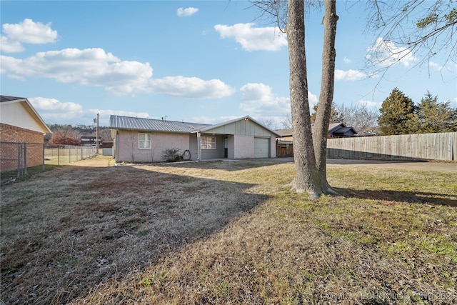 rear view of property featuring metal roof, a lawn, an attached garage, and a fenced backyard