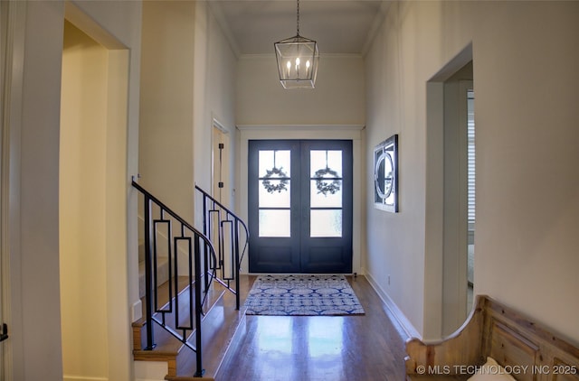 foyer with crown molding, a towering ceiling, wood-type flooring, french doors, and a chandelier