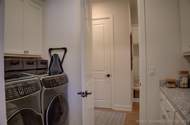 laundry area featuring cabinets, washing machine and dryer, and light hardwood / wood-style flooring