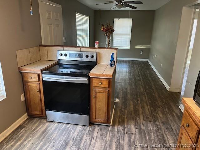 kitchen featuring dark hardwood / wood-style flooring, stainless steel electric stove, tile countertops, and ceiling fan