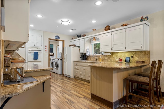 kitchen with white cabinetry, independent washer and dryer, light stone counters, and white appliances