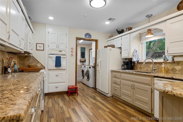 kitchen featuring washing machine and clothes dryer, sink, light stone counters, white appliances, and light hardwood / wood-style floors