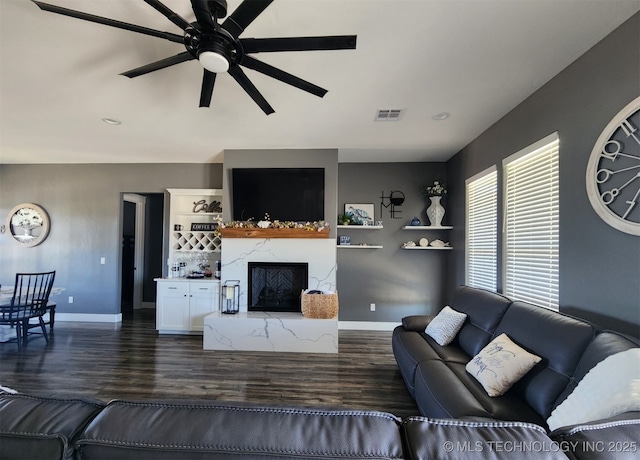 living room with dark wood-type flooring, ceiling fan, and a high end fireplace