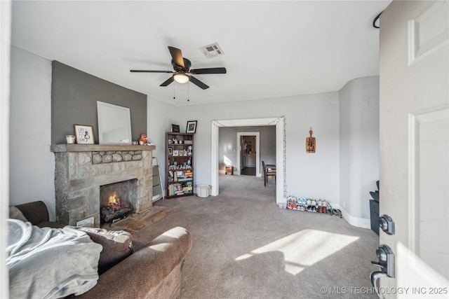 living room featuring ceiling fan, a stone fireplace, and carpet