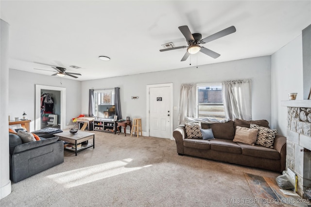 living room with ceiling fan, a healthy amount of sunlight, carpet flooring, and a stone fireplace