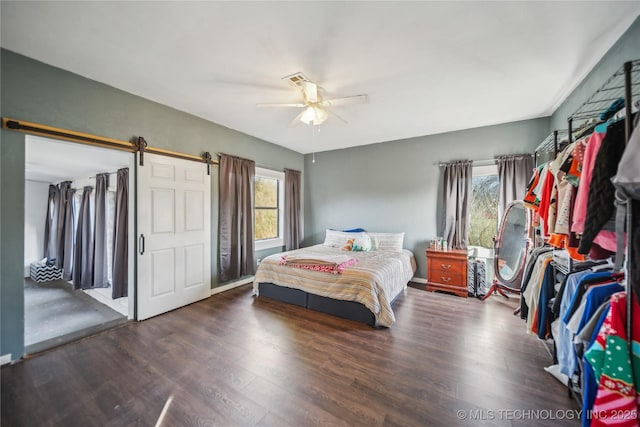 bedroom featuring ceiling fan, a barn door, dark hardwood / wood-style flooring, and multiple windows