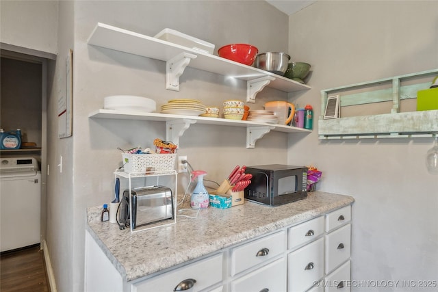 kitchen featuring light stone counters, washer / dryer, dark wood-type flooring, and white cabinets