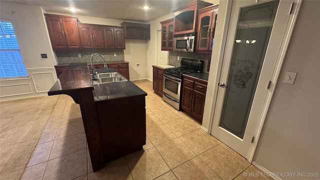 kitchen featuring an island with sink, sink, decorative backsplash, light tile patterned floors, and stainless steel appliances