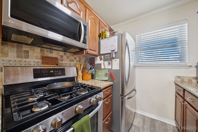 kitchen featuring crown molding, stainless steel appliances, light stone counters, tasteful backsplash, and light wood-type flooring