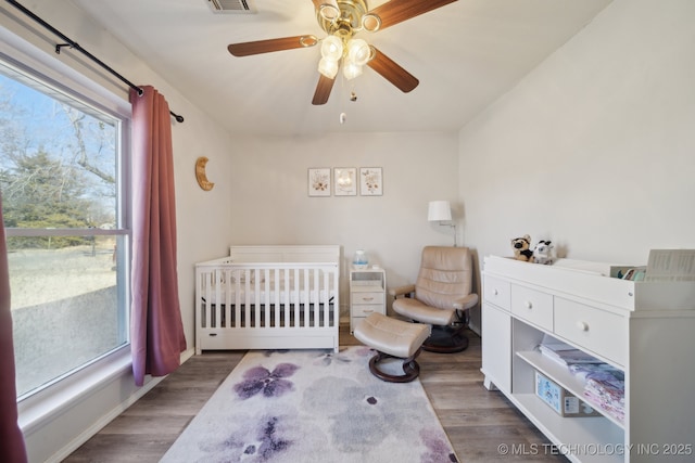 bedroom featuring a crib, dark wood-type flooring, and ceiling fan