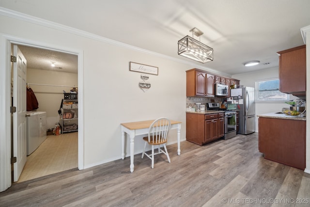 kitchen with washer and dryer, light wood-type flooring, appliances with stainless steel finishes, ornamental molding, and decorative backsplash