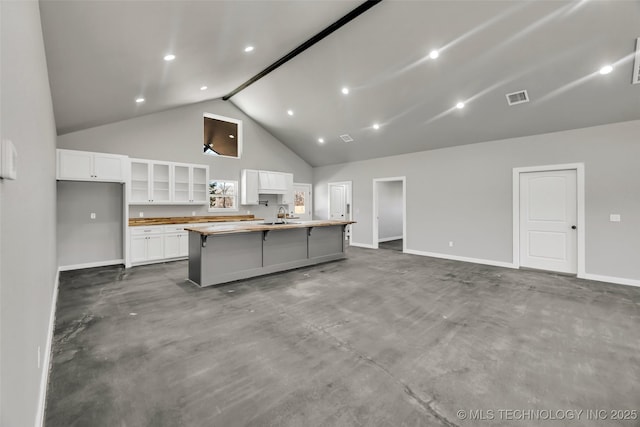 kitchen with sink, a breakfast bar area, high vaulted ceiling, a large island, and white cabinets