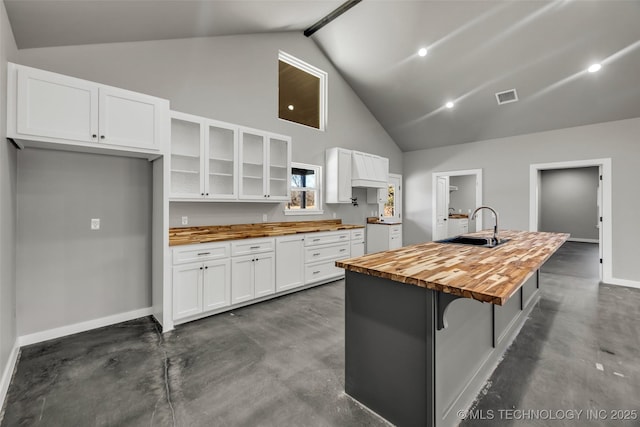 kitchen featuring high vaulted ceiling, butcher block countertops, white cabinetry, sink, and a center island with sink