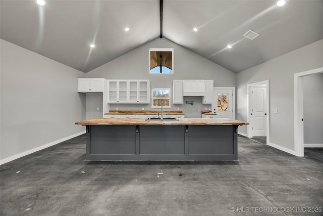 kitchen featuring a kitchen island with sink, butcher block countertops, white cabinetry, and a breakfast bar area