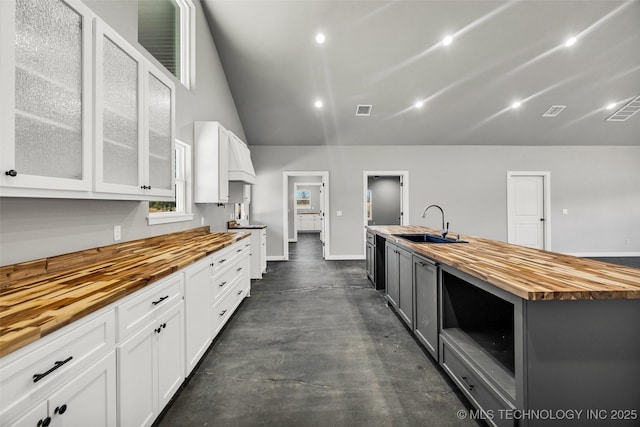 kitchen featuring sink, white cabinetry, wooden counters, vaulted ceiling, and a kitchen island with sink