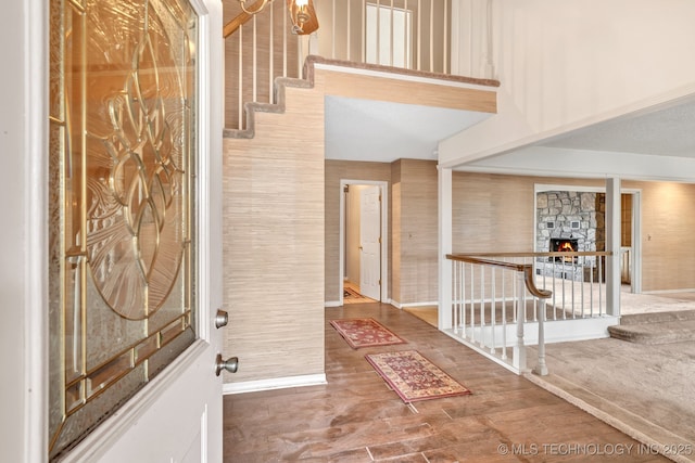 entryway with wood-type flooring, a stone fireplace, and a towering ceiling