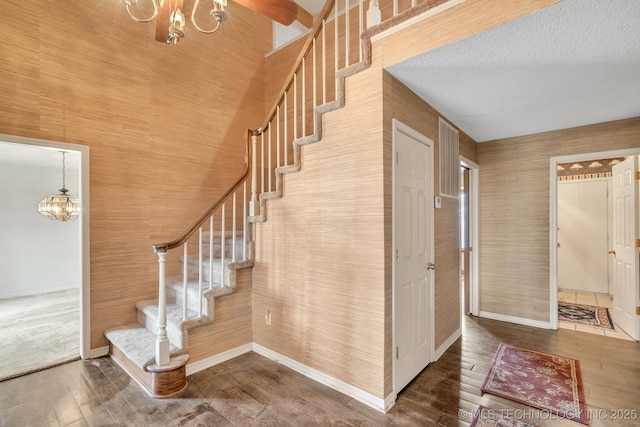 stairway featuring hardwood / wood-style floors, a textured ceiling, and a notable chandelier