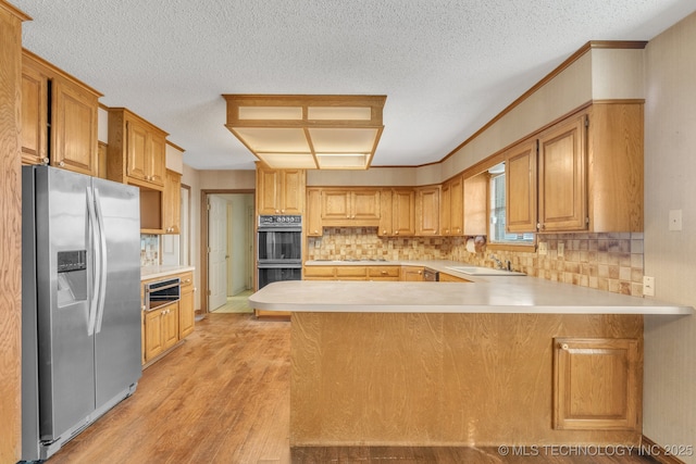 kitchen with sink, kitchen peninsula, double oven, and stainless steel fridge with ice dispenser