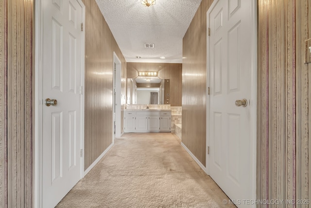 corridor featuring sink, light colored carpet, and a textured ceiling