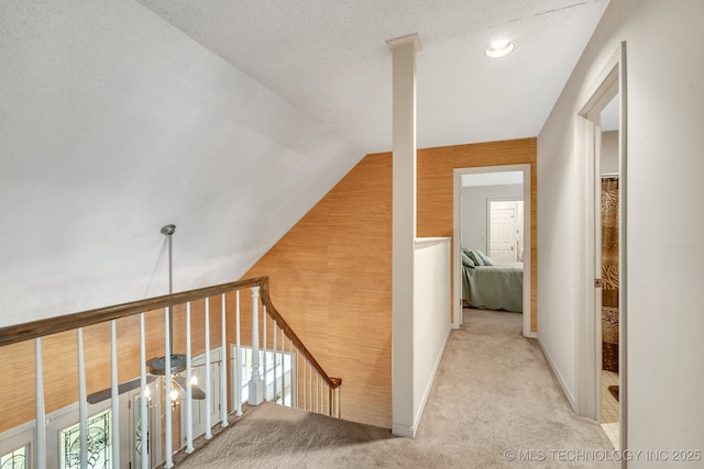 hallway featuring vaulted ceiling, light colored carpet, and a textured ceiling