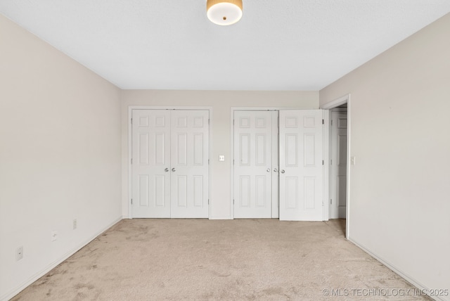 unfurnished bedroom with two closets and light colored carpet