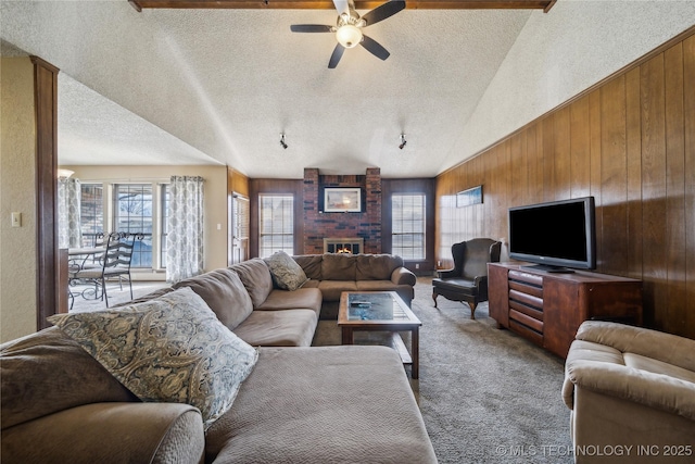 carpeted living room featuring wood walls, vaulted ceiling, a textured ceiling, ceiling fan, and a fireplace