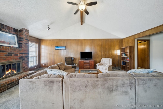 carpeted living room with vaulted ceiling with beams, a textured ceiling, a brick fireplace, wooden walls, and ceiling fan