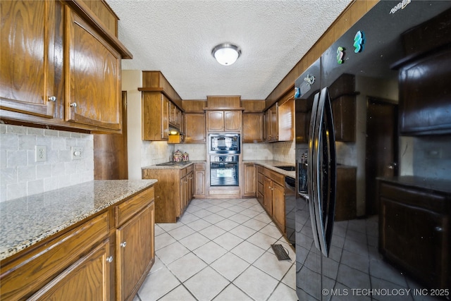 kitchen with light stone counters, tasteful backsplash, a textured ceiling, light tile patterned floors, and appliances with stainless steel finishes