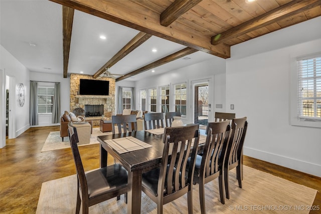 dining room featuring ceiling fan, a stone fireplace, and beam ceiling