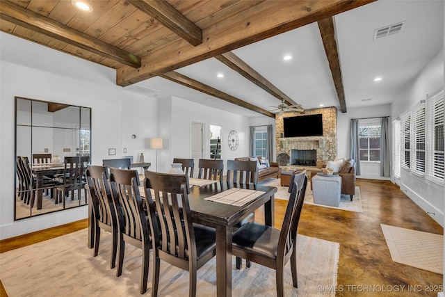 dining space featuring beam ceiling, concrete floors, wooden ceiling, ceiling fan, and a fireplace