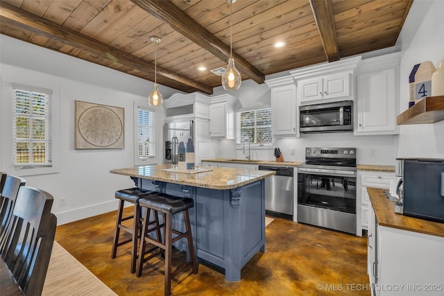 kitchen featuring decorative light fixtures, white cabinetry, stainless steel appliances, light stone countertops, and a center island with sink