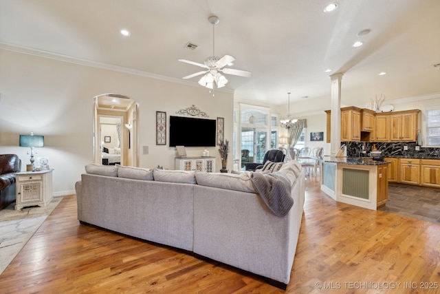 living room with ceiling fan with notable chandelier, ornamental molding, and light wood-type flooring