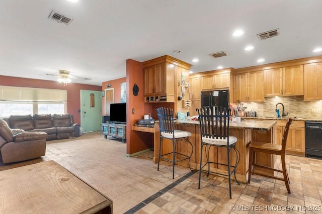 kitchen featuring sink, a kitchen breakfast bar, decorative backsplash, light stone counters, and black appliances