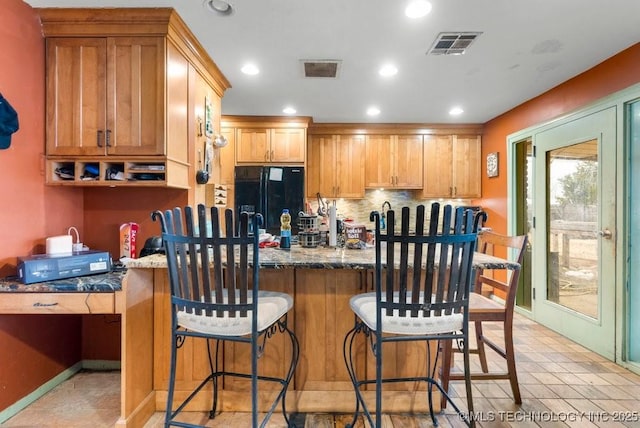 kitchen with dark stone countertops, backsplash, black fridge with ice dispenser, and a kitchen bar