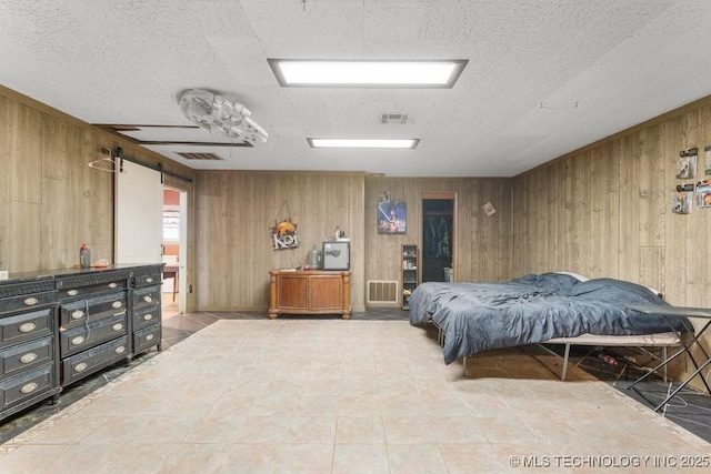 bedroom with a barn door, a textured ceiling, and wood walls