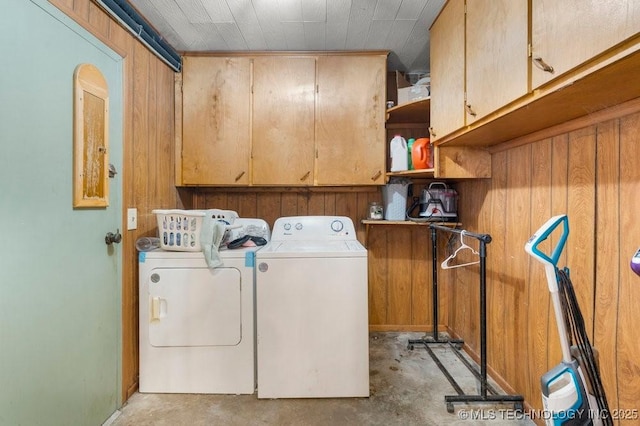 clothes washing area with wooden walls, washing machine and dryer, and cabinets