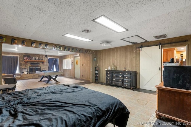 bedroom with a stone fireplace, wooden walls, and a barn door