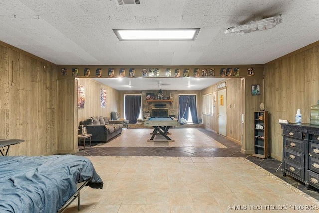 bedroom with wooden walls, a stone fireplace, and a textured ceiling